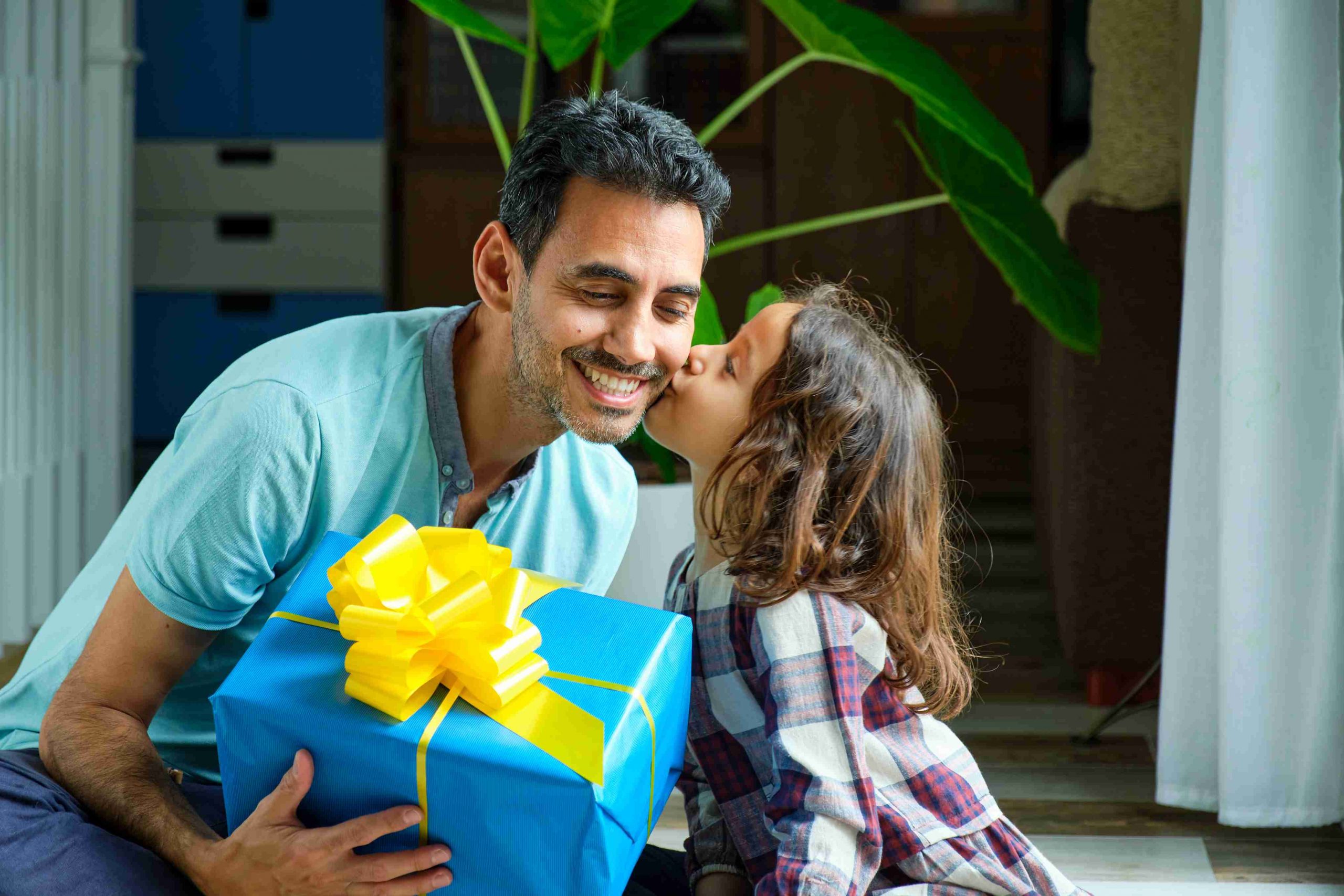 little girl giving father a kiss who is holding gift box in his hands