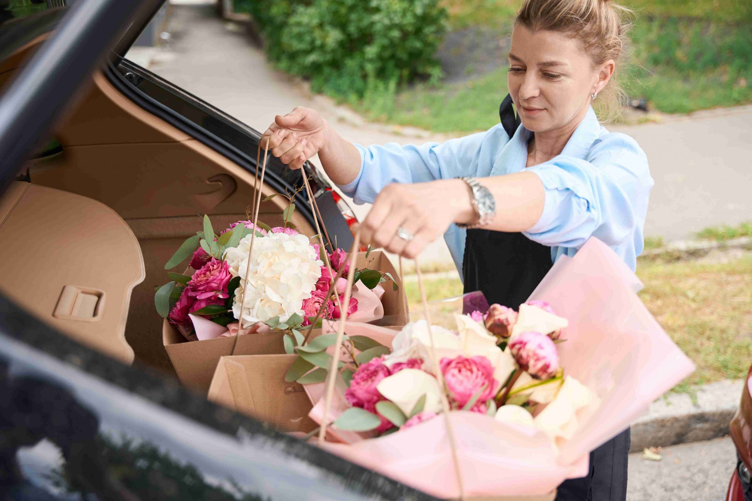 woman putting bouquet of flowers in car trunk