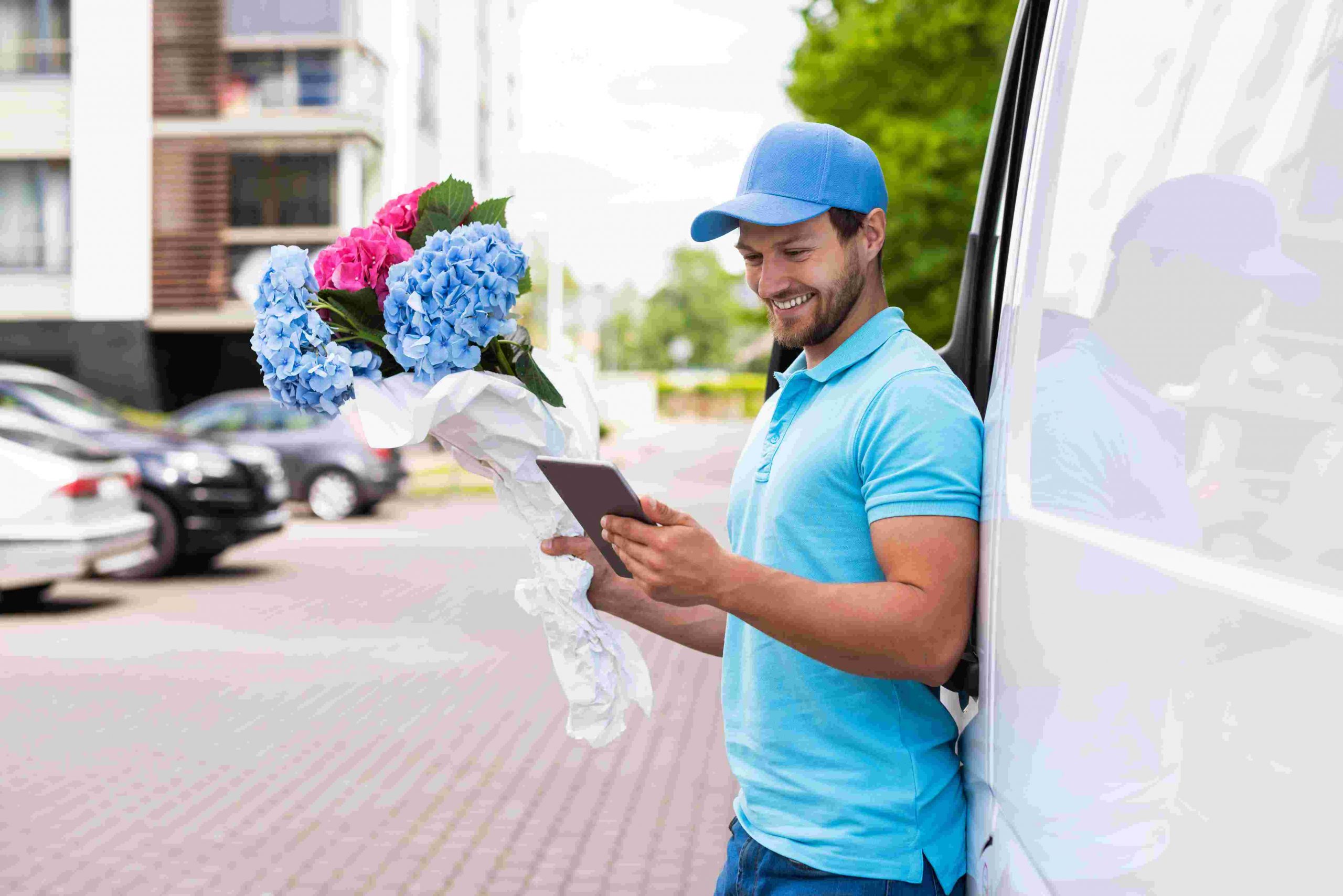 smiling courier with phone and flower bouquet during flower delivery