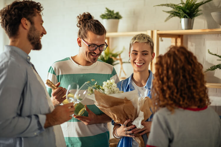 group of friends smiling at one another and holding flowers