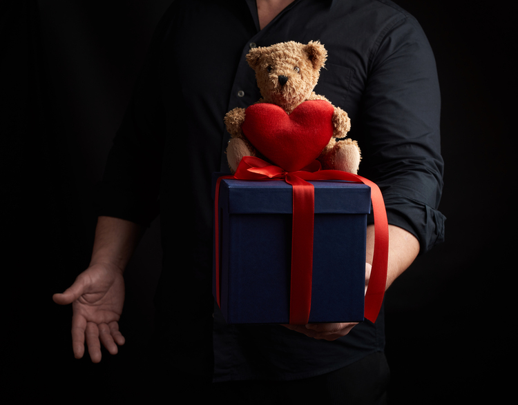 valentines day gifts for him: adult man in back shirt holding square box and teddy bear